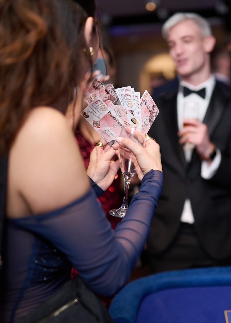 Charity casino night: guest holding a fan of Royale fun-money notes at a black-tie fundraiser
