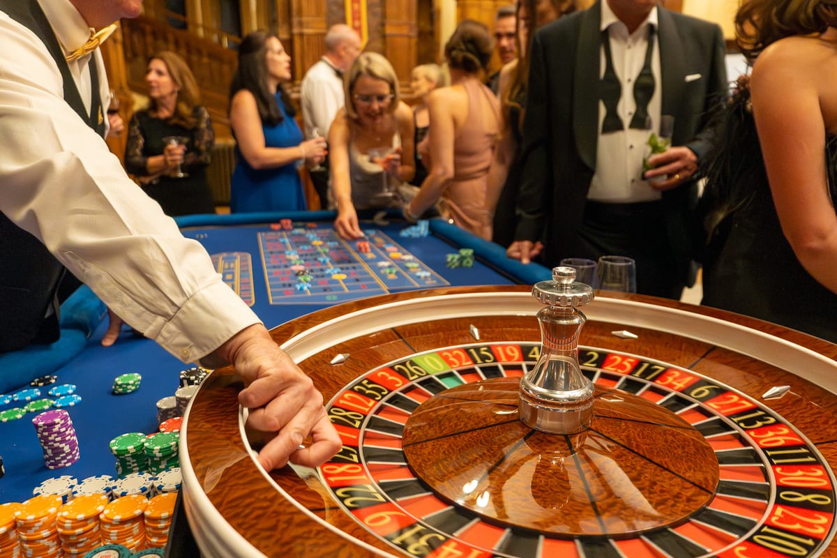 A croupier spins the wheel as guests in black tie look on in an oak-panelled hall